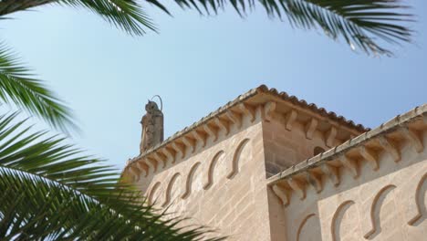 looking up to small statute of lady of mount carmel on top roman catholic church in porto cristo, palm tree leaves moving in slow wind foreground