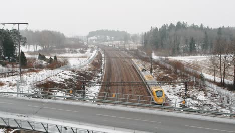 Aerial-shot-of-a-speed-train,-Arlanda-Express-passing-by-under-drone-in-industrial,-winter-landscape-going-towards-Arlanda-Airport