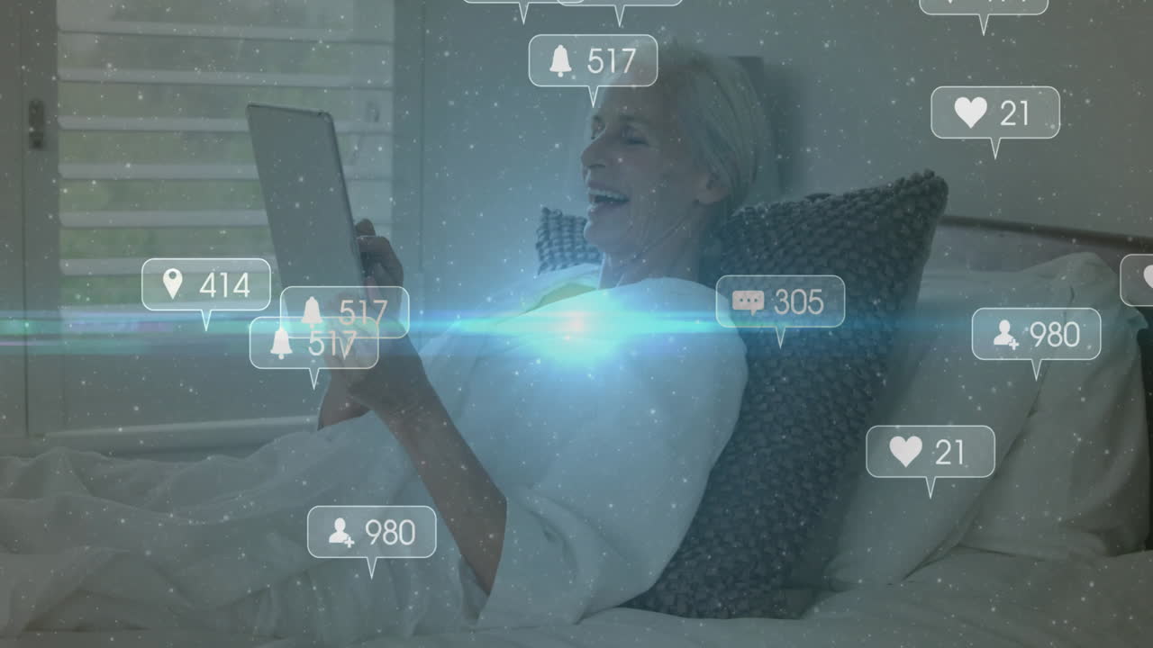 Using tablet in bed, elderly woman viewing animation of social media notifications