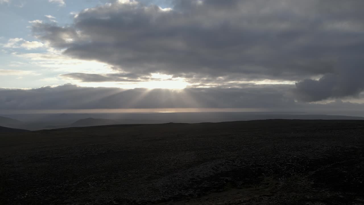 From a mountain's peak, the sun breaks through the clouds, a divine interaction of light and shadow over the rugged terrain, showcased in 4K