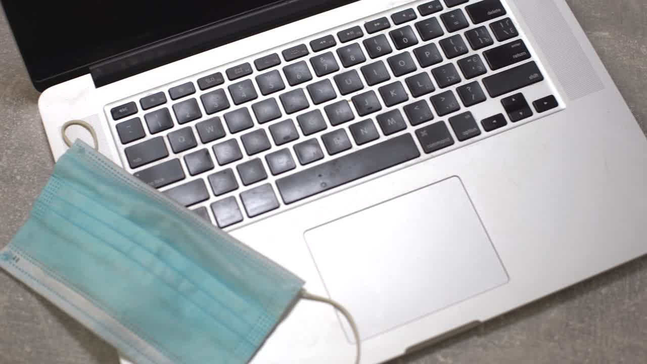 의료 얼굴 마스크, 노트패드 및 펜을 가진 노트북 컴퓨터와 함께 식탁에 커피 한 잔. 가정 설정. 집에서 일하는 개념.