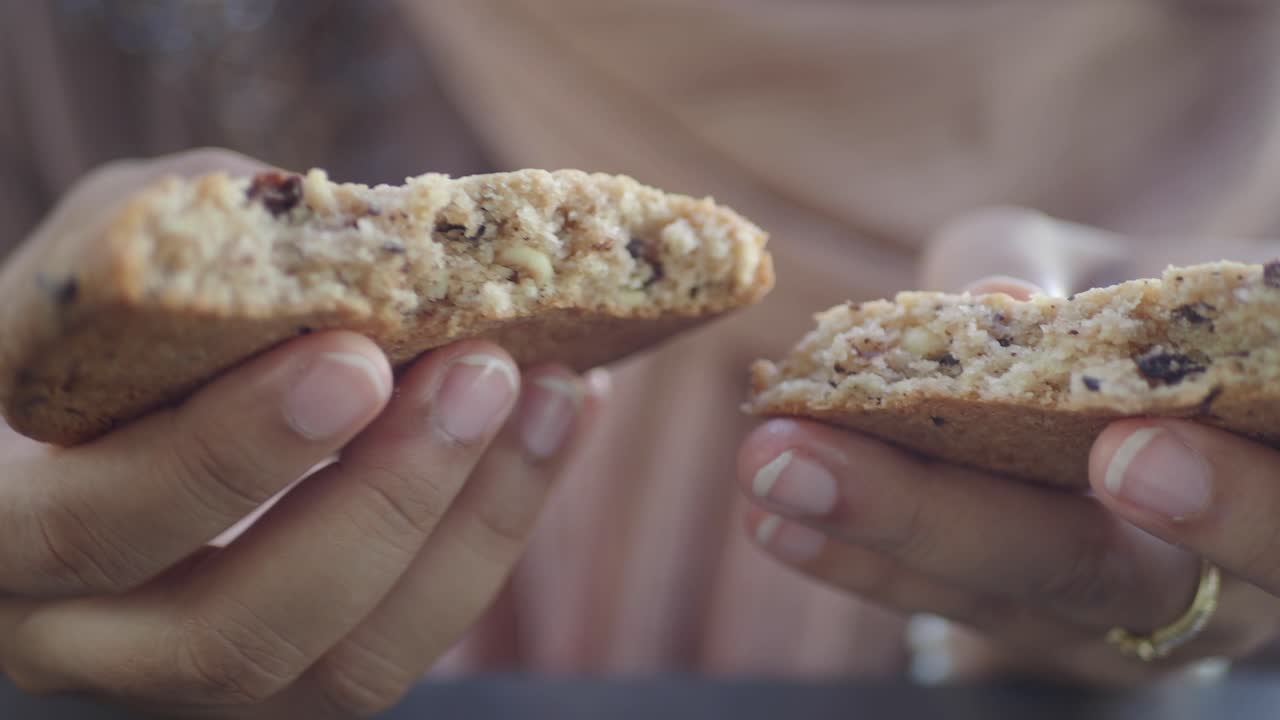 Primo piano di mani che tengono un biscotto rotto con gocce di cioccolato