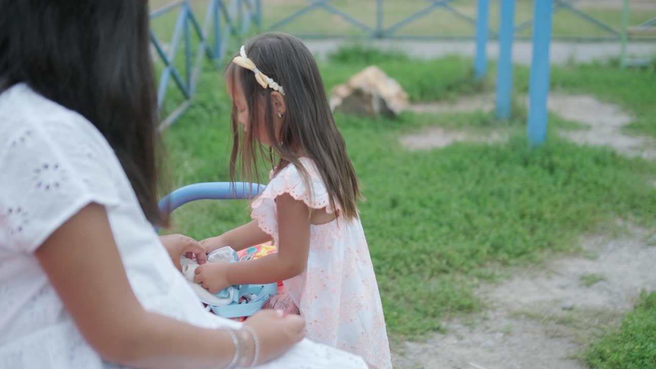 임신 한 어머니 와 어린 딸 은 나무 와 초록색 으로 둘러싸인 공원 의 놀이터 에서 함께 놀이 를 즐긴다