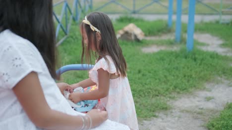 una madre embarazada y su hija joven disfrutan de un tiempo de juego juntos en un patio de recreo en el parque, rodeados de árboles y vegetación
