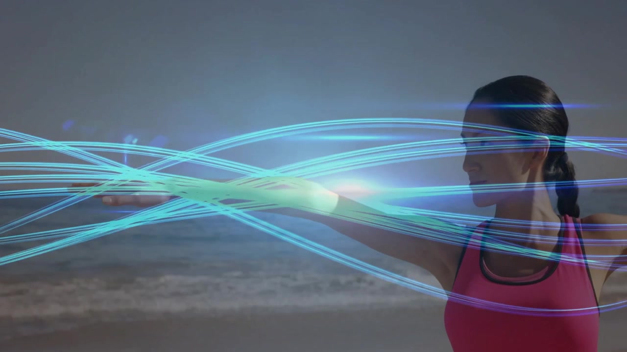 Donna che alza le braccia sopra la testa attivando scie luminose mentre esegue uno stretching laterale per il fitness su una spiaggia sabbiosa.