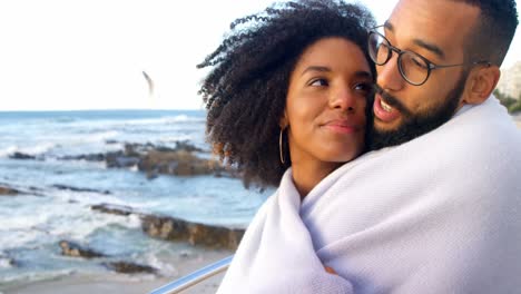 Couple-in-blanket-embracing-each-other-at-beach-4k