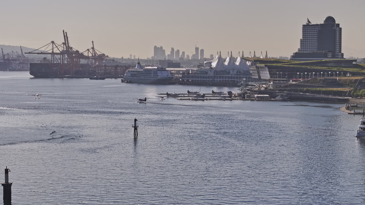 Vancouver BC Canada Aerial v87 zoomed view drone flyover the harbour capturing seaplane landing on the water against shipyard and waterfront downtown cityscape - Shot with Mavic 3 Pro Cine - July 2023