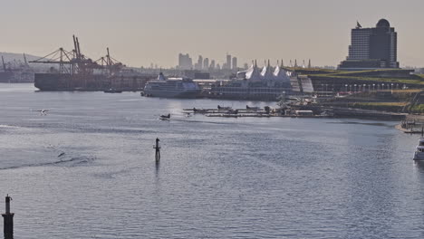 Vancouver-BC-Canada-Aerial-v87-zoomed-view-drone-flyover-the-harbour-capturing-seaplane-landing-on-the-water-against-shipyard-and-waterfront-downtown-cityscape---Shot-with-Mavic-3-Pro-Cine---July-2023