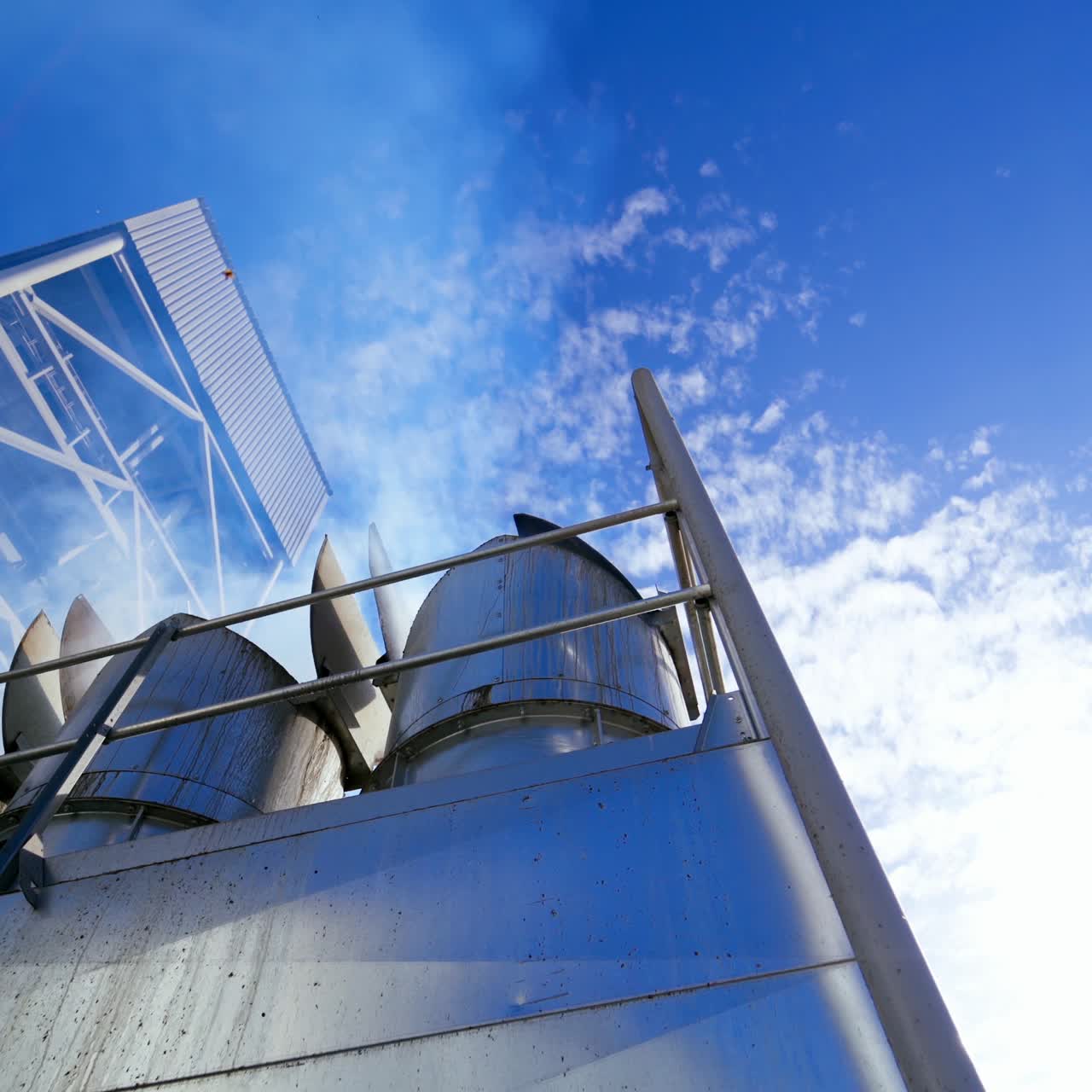 Exterior of warehouse at sunlight. White smoke go into the air from metal pipes of modern granary. Industrial equipment for agribusiness. View from below.