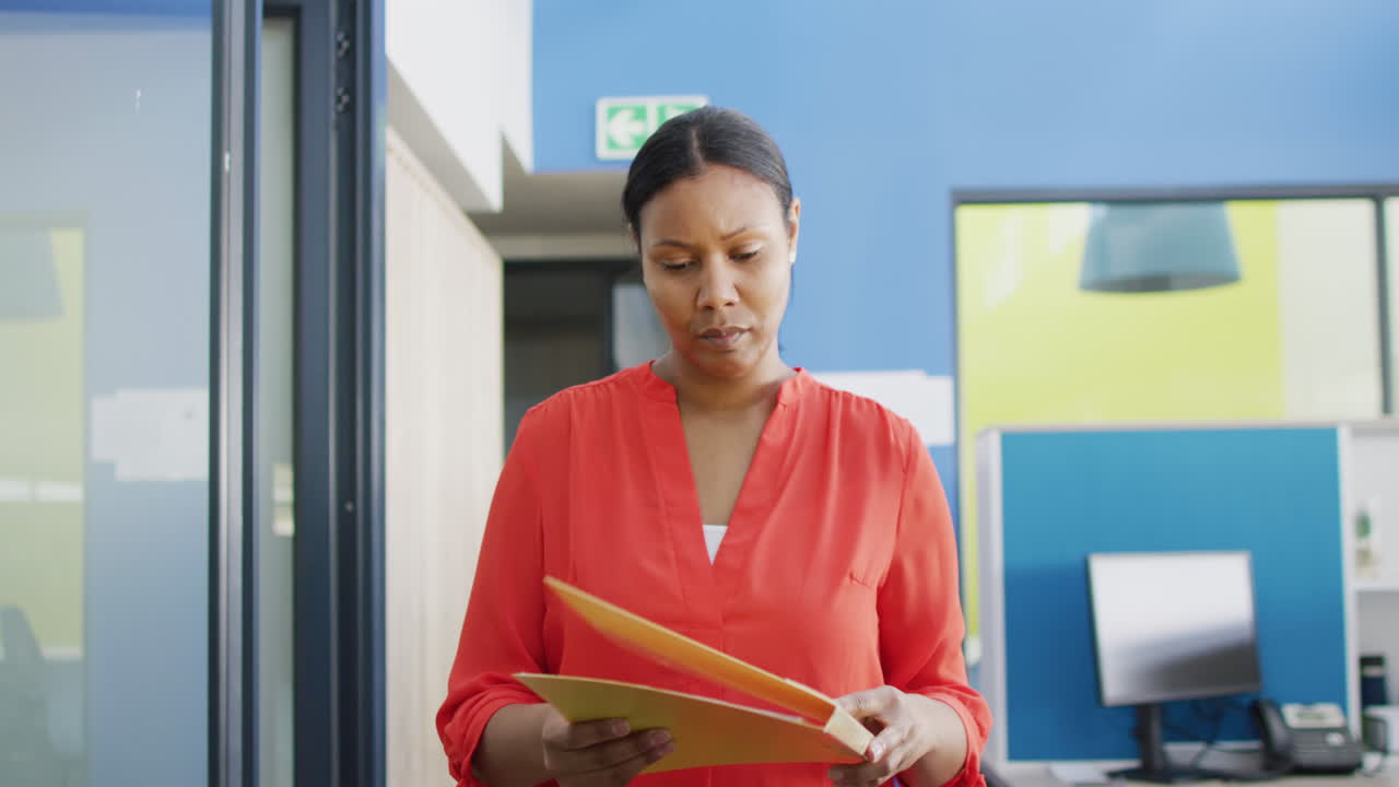 African american businesswoman walking and holding documents at office, slow motion