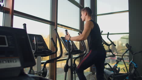 Un-Hombre-De-Fitness-Retrato-Se-Calienta-Antes-De-Entrenar-En-Una-Bicicleta-Elíptica-En-El-Gimnasio.-Ejercicio-Cardiovascular-De-Entrenamiento-Masculino-De-Primer-Plano-En-Bicicleta-Cruzada-En-Fitness