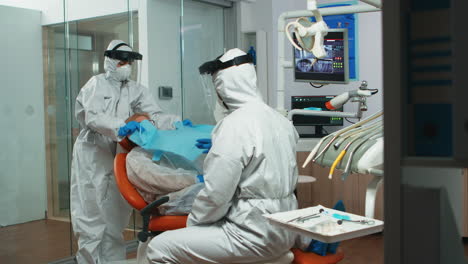 Nurse-in-coverall-putting-dental-bib-to-woman-during-examining