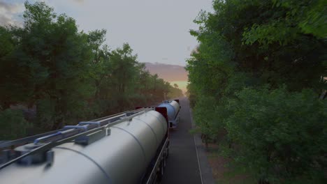 two gasoline tanker semi truck on asphalt road. silver fuel semi truck fast driving on straight freeway in countryside dense forest