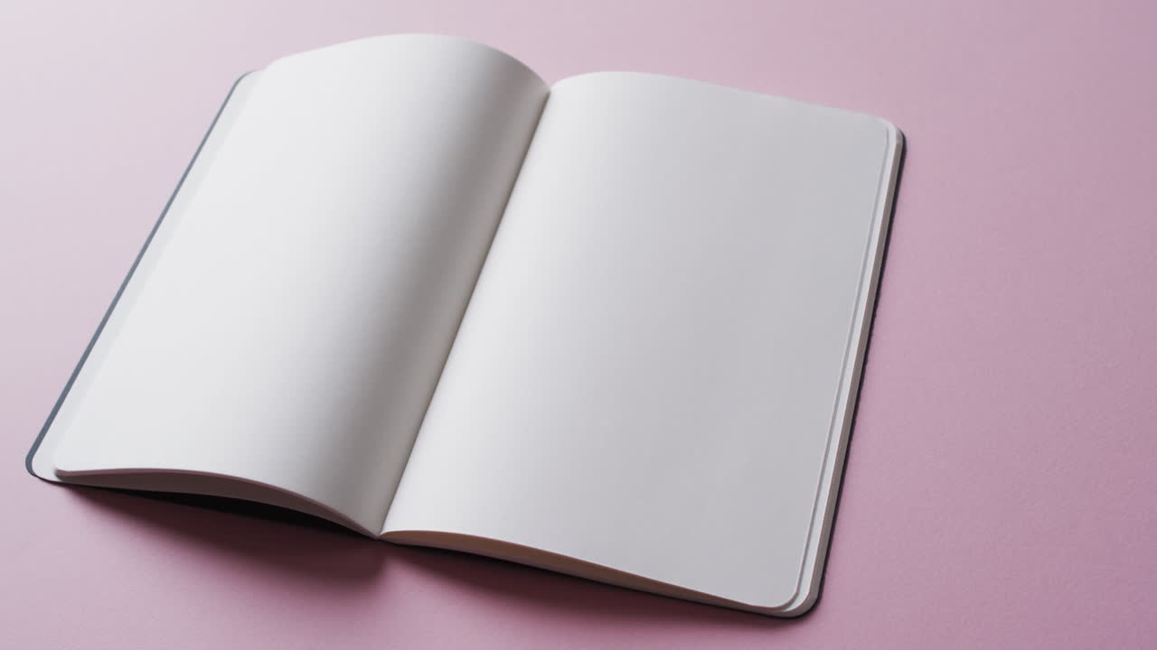 Close up of open blank book with copy space on pink background in slow motion
