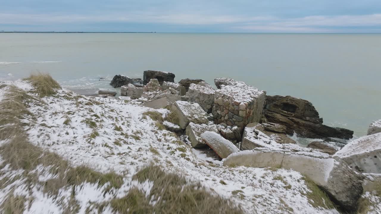 Aerial establishing view of abandoned seaside fortification buildings at Karosta Northern Forts on the beach of Baltic sea , overcast winter day, wide drone shot moving forward