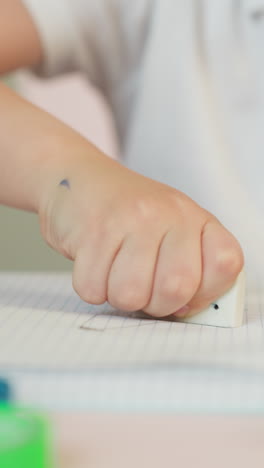 little student removes bad picture with eraser from exercise book page at desk closeup. toddler boy unsatisfied by drawing fail at art lesson