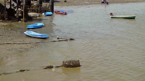 an establishing shot of small blue plastic boats moored in the shallow waters during low tide at a traditional fishing town in si racha, thailand