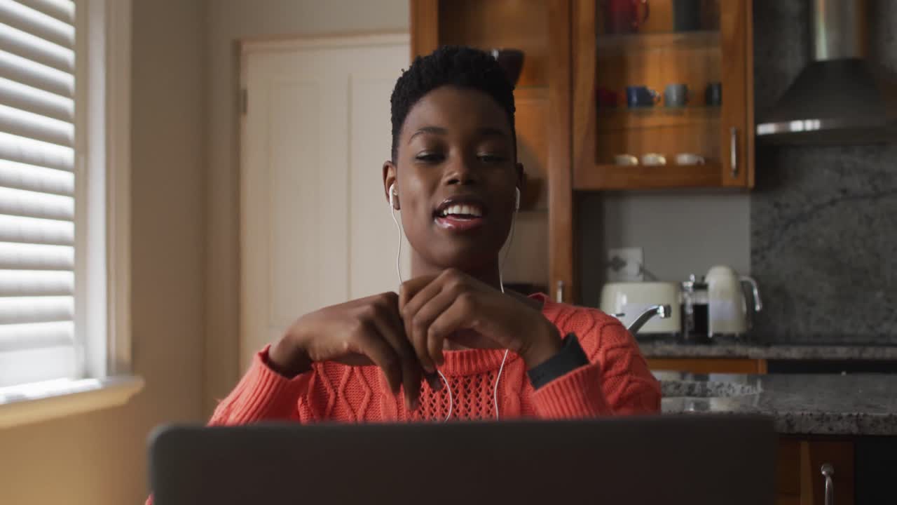 African american woman wearing earphones having a videocall on laptop while working from home
