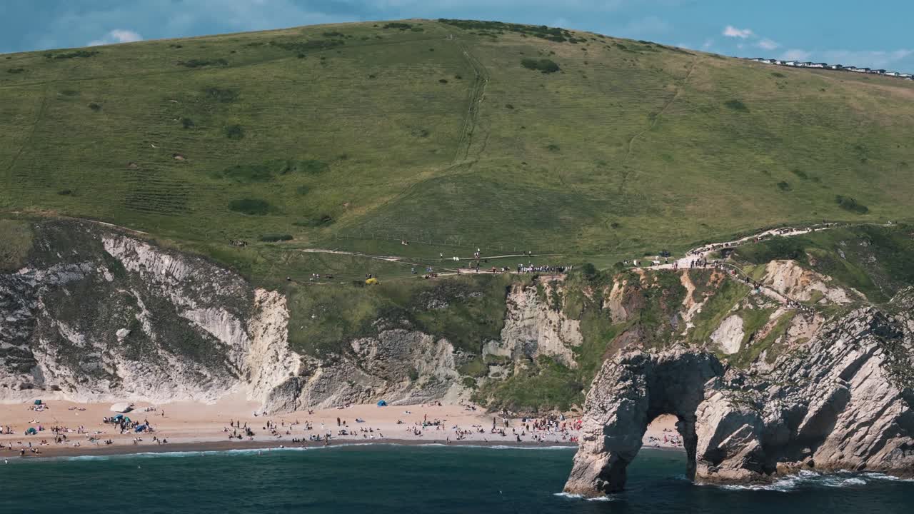 Dolly right revealing beach at Durdle Door framed by dramatic cliffs and lush hills