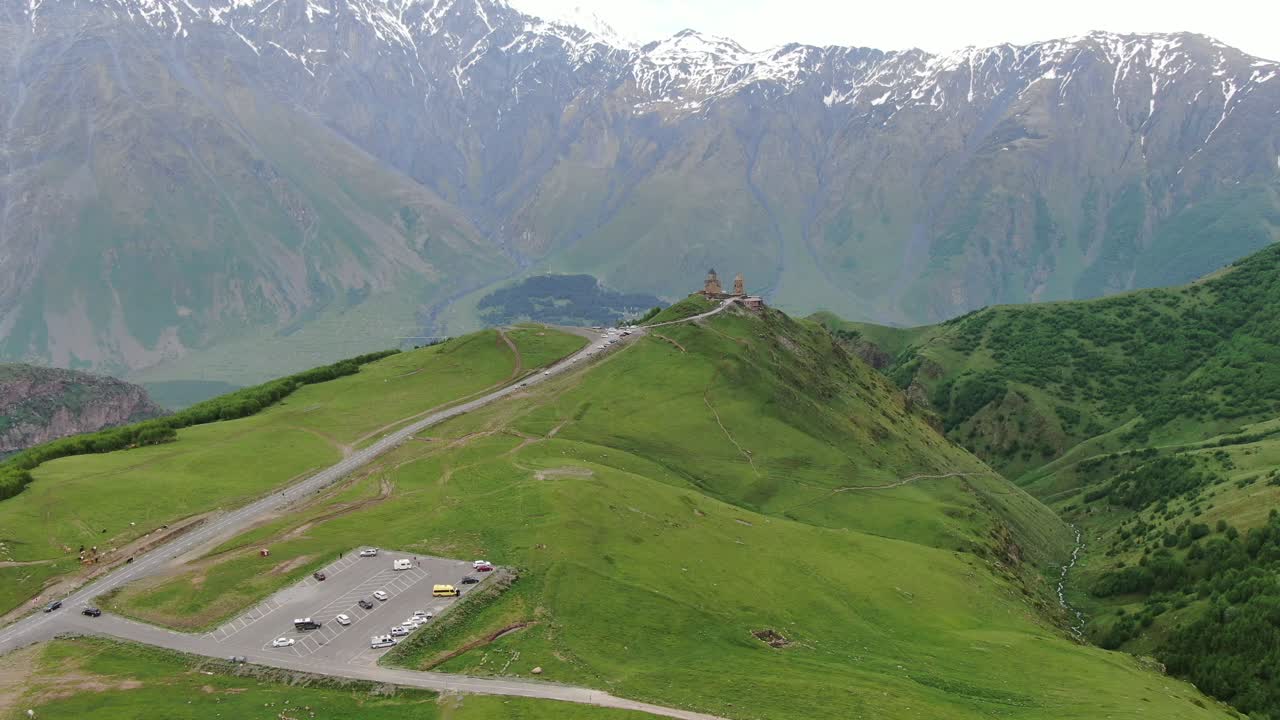 vista aérea de un avión no tripulado en georgia volando hacia la iglesia ortodoxa de la trinidad de gergeti en kazbegi rodeada de montañas verdes valle con picos nevados