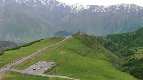 vista aérea de un avión no tripulado en georgia volando hacia la iglesia ortodoxa de la trinidad de gergeti en kazbegi rodeada de montañas verdes valle con picos nevados