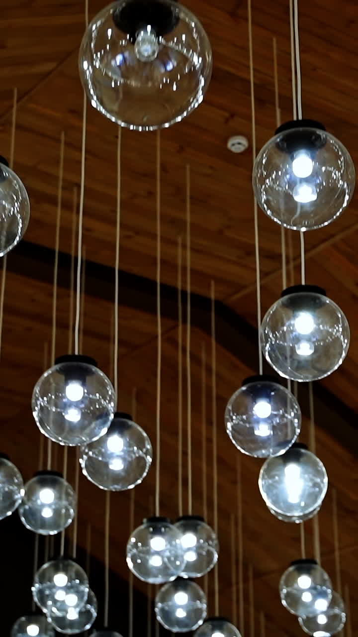 Modern ceiling design. Shining glass balls hanging from the top. Interior of glowing round lamps on white wires. Vertical video