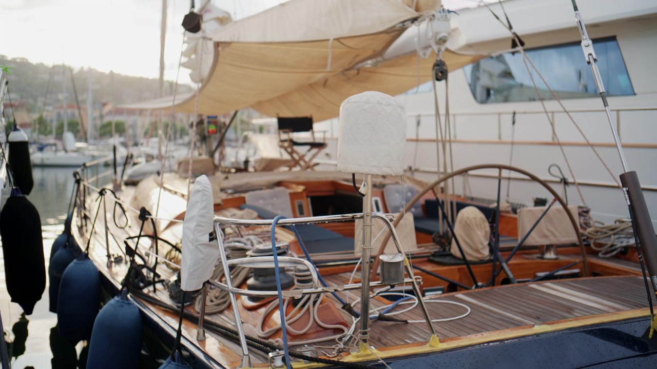 Scatto serale caldo del ponte di una classica barca a vela in legno ormeggiata al porto turistico di Port Vauban ad Antibes, con cime, vele coperte, legno lucidato e yacht di lusso nelle vicinanze