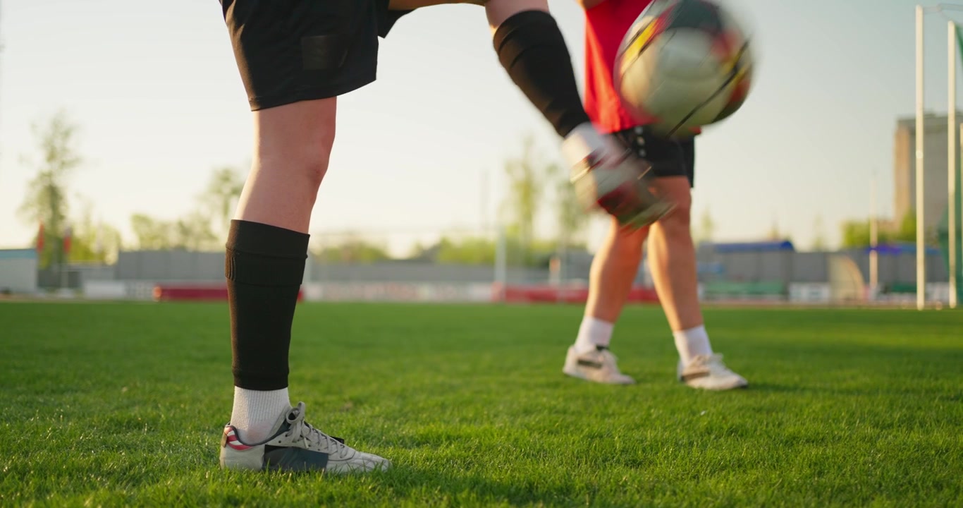 緑のフィールドでボールを使ってトレーニングするサッカー選手の足元のクローズアップ
