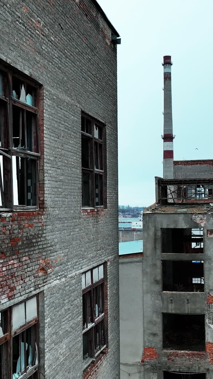 Old brick and concrete premises of an abandoned factory. Huge industrial territory with ruined constructions at the backdrop of a city. Vertical video