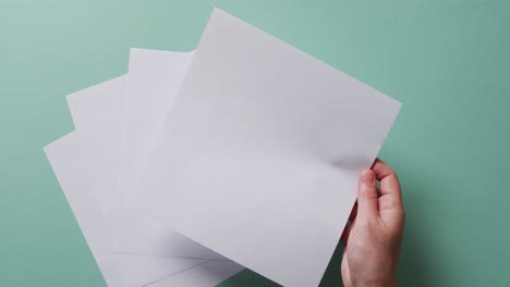 mano sosteniendo un pedazo de papel sobre pedazos de papel con espacio de copia en fondo verde en cámara lenta