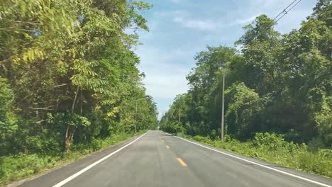 driver's view of a scenic road trip in the countryside of thailand surrounded with green foliage and trees