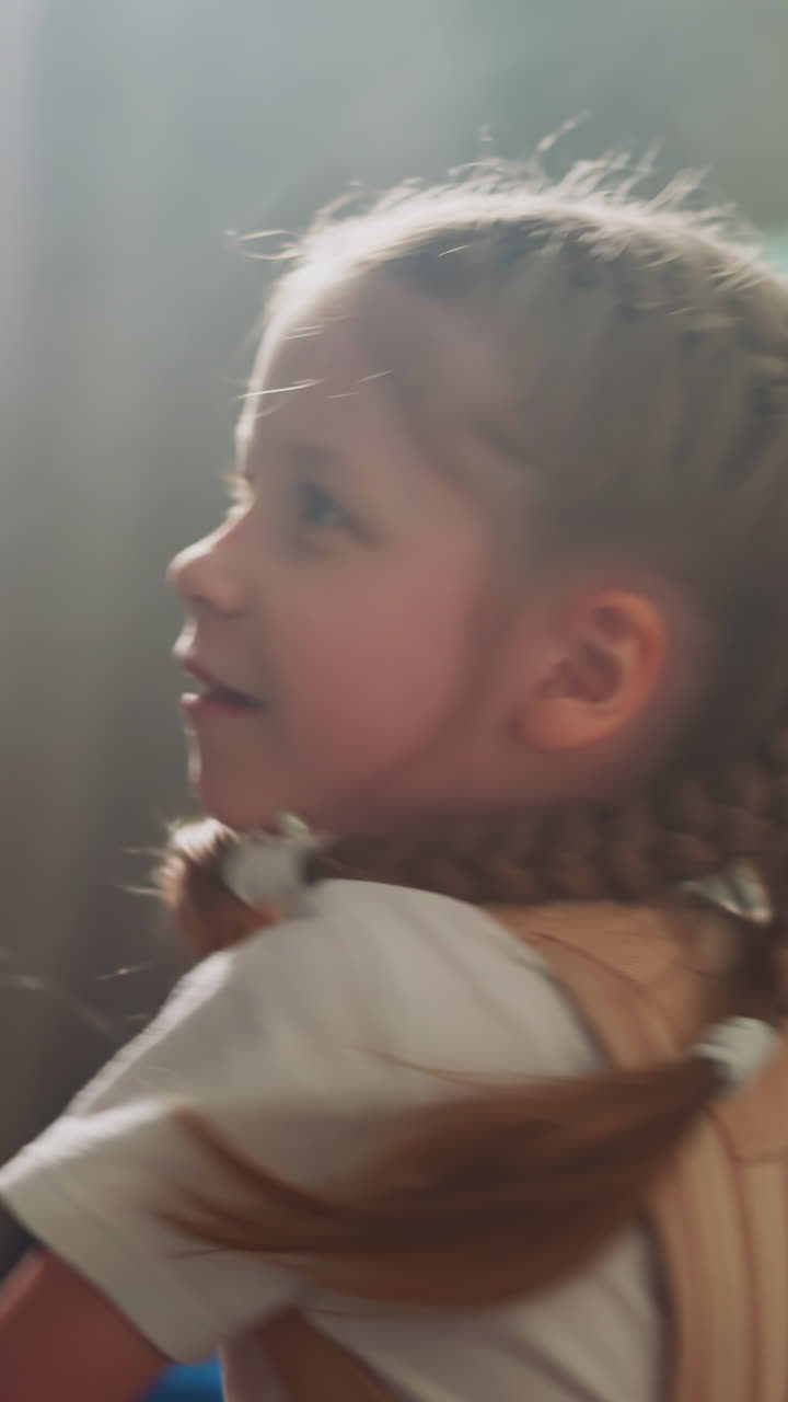 Happy little girl with back brace punches swinging boxing bag in playing room slow motion. Smiling child undergoes rehabilitation after spine injury