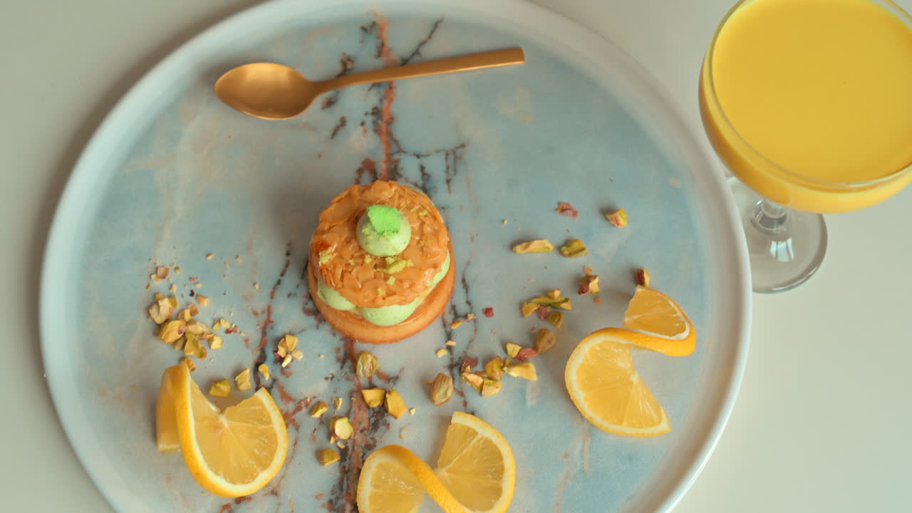 Primer plano de un postre de pistacho con rodajas de limón en un plato cerca de un vaso de zumo de naranja