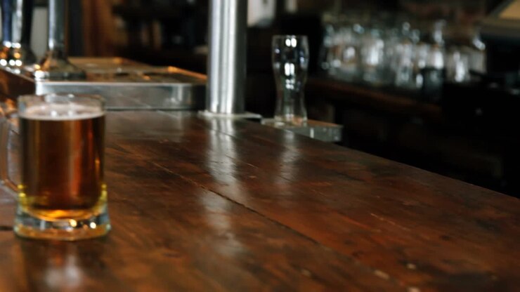 Campo lungo che mostra una donna al bar che si gira verso un uomo mentre chiacchiera amichevolmente con delle birre e coriandoli dorati che fluttuano