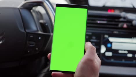 mano cercana del conductor en el coche utiliza un teléfono inteligente con una pantalla verde, dentro de un coche. versión 2