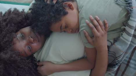 loving mother lying on bed and embracing sleeping son