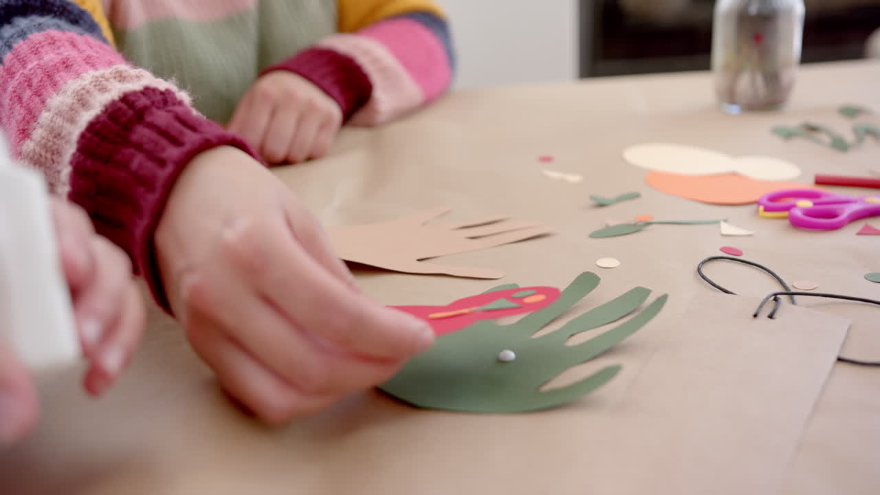 madre y hija bi-raciales felices pegando recortes coloridos en la sala de estar soleada