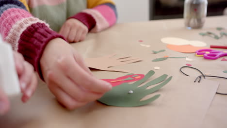 Happy-biracial-mother-and-daughter-sticking-colourful-cutouts-in-sunny-living-room