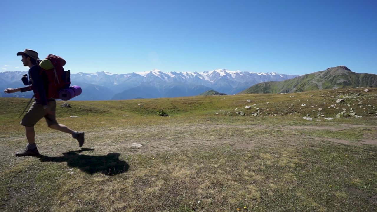 Hiker cross the frame from right to left in nature, snow mountain background