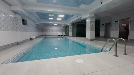 clean tiled indoor pool with calm water, lounge chairs, and ambient lighting in a spa-like setting