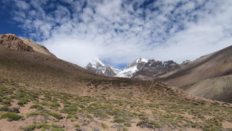 view of the summit of aconcagua from the approach to basecamp, with blue sky and clouds moving over the mountains creating shadows in the valley