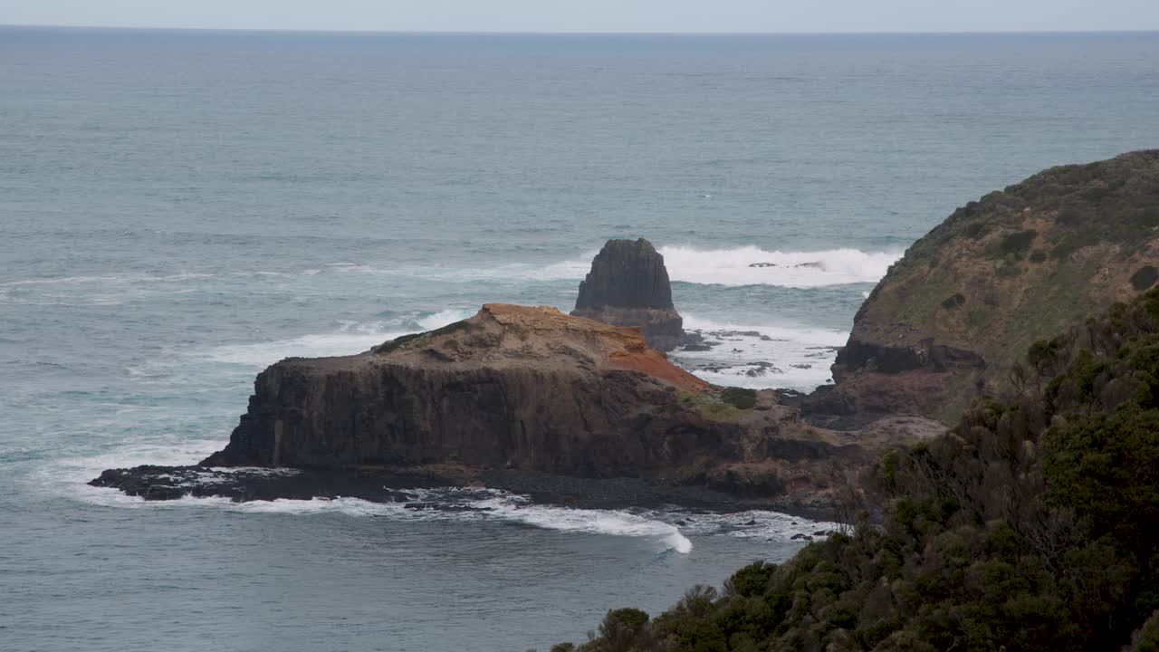 Steady wide shot of rugged cliffs, ocean waves, and overcast sky at Cape Schanck coastline