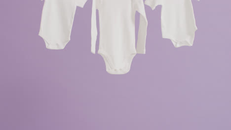 Video-of-close-up-of-three-white-baby-grows-hanging-on-purple-background