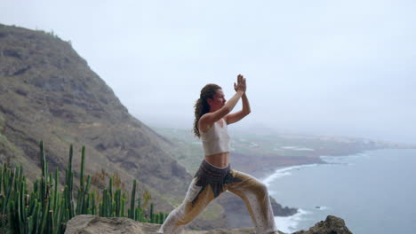 At-sunset-on-a-rocky-seashore,-a-young-woman-engages-in-yoga,-symbolizing-a-healthy-lifestyle,-harmony,-and-the-intricate-connection-shared-between-humans-and-the-blue-ocean-backdrop