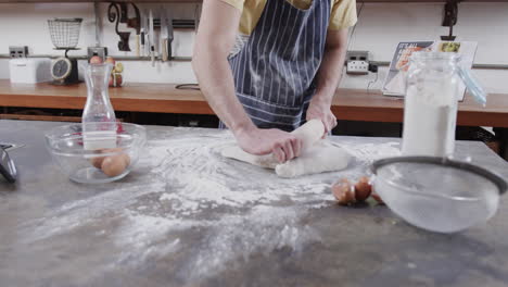 Midsection-of-caucasian-man-preparing-bread-dough-using-tablet-in-kitchen,-slow-motion