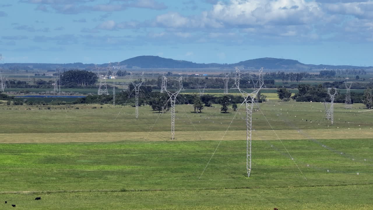 Transmission towers create lateral parallax across open fields, emphasizing large scale grid infrastructure and high voltage power distribution