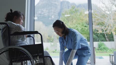 asian female doctor talking to female patient in wheelchair and arranging her feet at hospital