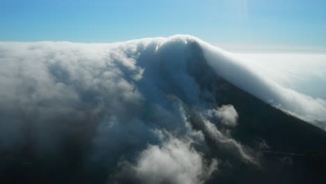 aerial shot of a mountain completely covered in clouds which evaporate when they go over the mountain in cape town, south africa