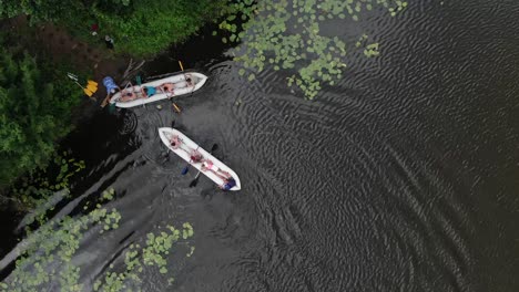 aerial birds-eye view of two canoes filled with people in a river docking on shore