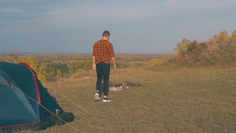 guy in orange shirt goes out of tent and walks to bonfire